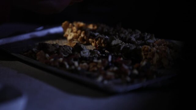 Close-up of hands stringing walnuts on thread for traditional Georgian dessert Churchkhela. Authentic homemade preparation process arranging nuts on a metal tray in a cozy kitchen setting.

