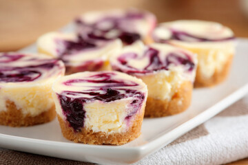 Mini blueberry swirl cheesecake bites served on a white plate with a kitchen background showcasing a delicious homemade treat