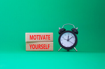 Motivation symbol. Concept words Motivate yourself on wooden blocks. Beautiful green background with alarm clock. Business and Motivate yourself concept. Copy space.
