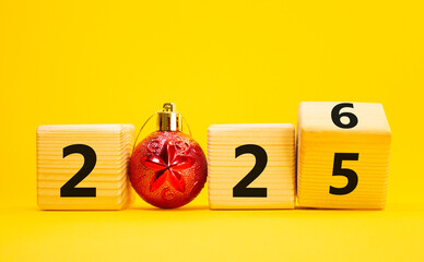 2026 New Year symbol. Businessman turns wooden cube and changes Year 2025 to 2026. Beautiful yellow background with Christmas ball. Copy space. Business and 2026 happy new year concept