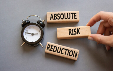 Absolute Risk Reduction symbol. Concept words Absolute Risk Reduction on wooden blocks. Businessman hand. Beautiful grey background with alarm clock. Business  concept. Copy space.