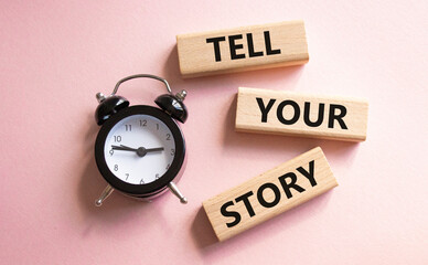 Tell your story symbol. Wooden blocks with words Tell your story. Beautiful pink background with alarm clock. Business and Tell your story concept. Copy space.