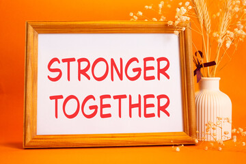 Stronger together symbol. Concept words Stronger together on beautiful wooden picture frame. Beautiful orange background with flower vase. Business and Stronger together concept. Copy space.
