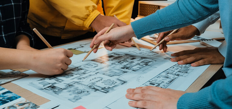 A collaborative design session where a diverse group engages with sketches and blueprints on a table, showcasing teamwork and innovative planning in an inspiring workspace. SACTR