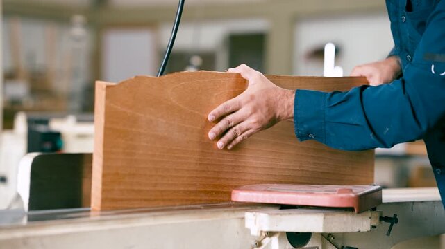 Close up of a skilled carpenter's hands guiding a wooden plank through a jointer machine, precisely shaping the wood in a workshop setting