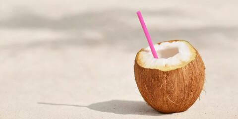 Coconut drink with pink straw on sand enjoying tropical summer beach vacation and holiday vibes