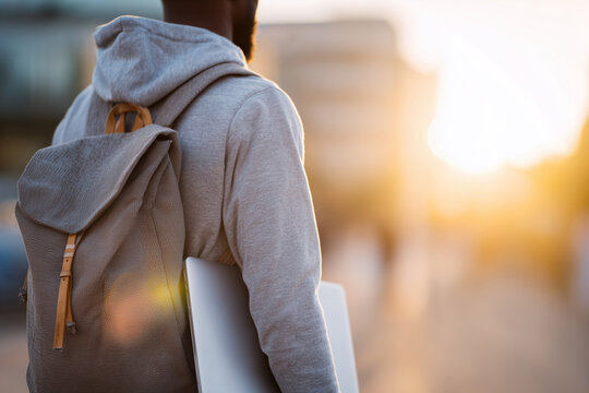 A man wearing a gray hoodie and backpack is walking down a street