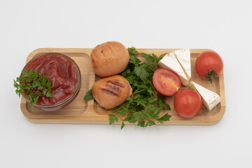 Close up of grilled sausages with tomatoes, soft cheese, parsley and tomato sauce on wooden board. Homemade meal isolated on white background.