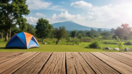 Empty rustic wooden table with blurred camping tent, green field, and mountain background on a sunny day.