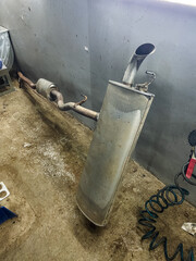 disassembled exhaust system on concrete ground, car exhaust muffler disassembly with scattered components and stains, broken exhaust muffler lying on floor amid oil stains and disorganized parts