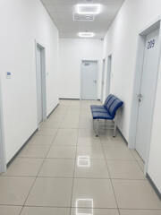 Bright modern hospital corridor with white walls, blue chairs and numbered consultation room doors