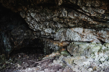 Sheltered cave alcove with pebblecovered floor and low overhang, dim shadows, textured limestone walls and scattered debris creating secluded protective niche ideal for refuge or nature