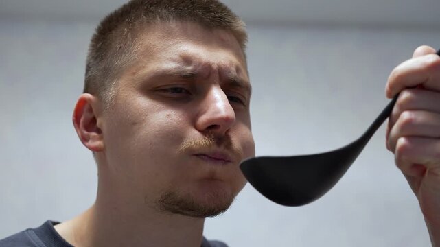 A guy is holding a ladle over cooked food in the kitchen.
Preparing hot food.
The cooking process.
The guy is tasting the food, checking for salt and spices.
Hot, delicious food.