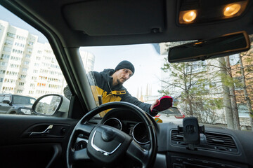 cleaning windshield before journey, man wiping car windshield in city background, person preparing vehicle by wiping windshield amidst cityscape to ensure safe travel readiness