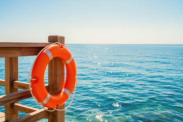 Orange lifebuoy on wooden railing by blue sea