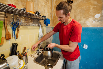 man washing dishes energetically, cooking area maintenance with man diligently washing utensils, individuals engaged in cleaning and organizing kitchen during lively household activity