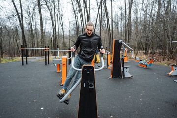 athletic individual performing core exercises at city park amid autumn scenery, male athlete executes leg lifts on parallel bars during outdoor urban fitness session in fall surroundings