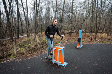 white man monitoring workout on stepper machine in park, attentive posture, muted autumn palette, focus on metrics and steady training habit, device and motion details visible
