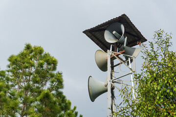 Loudspeakers on Tower Surrounded by Green Trees Against Gray Sky