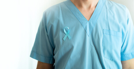 Close up of male doctor wearing medical uniform with blue satin ribbon. Banner isolated on white. November prostate cancer awareness month concept, prevention, early diagnosis, and oncology treatment