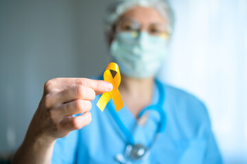 A woman medical staff holds a yellow satin ribbon, emblem for sarcoma, childhood cancer, suicide...