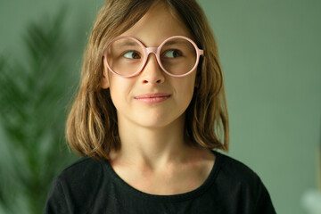 Close up portrait of a little girl in round glasses looking away with mischievous squint and smile. Emotions of curiosity, cleverness and childhood insight.