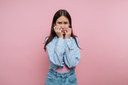 Young person expressing discomfort in front of a pink background with a worried facial expression and hands covering mouth
