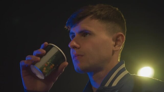 night street portrait caucasian man drinking coffee under neon lights, varsity jacket profile and closeup shots, contemplative pause between drives, steam rising from cup, amber bokeh from distant
