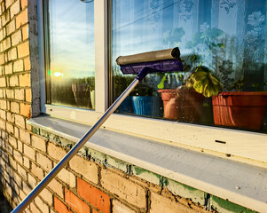 Window cleaning. Window cleaning tools. Applying soapy water to the window glass, reflecting sunlight and houseplants through the glass, and demonstrating household cleaning techniques.