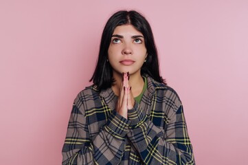Fototapeta premium Young woman with hands together looking up against a pink background in a casual outfit during indoor time