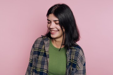 Fototapeta premium Young woman smiles while wearing a colorful shirt against a pink background during a casual indoor setting in the afternoon