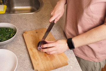 Woman chopping red onion on a wooden cutting board beside a bowl of frozen green beans in a cozy kitchen, preparing vegetables for a hot homemade dish for recipe blogs and family dinner ideas