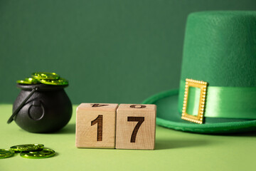 St Patricks day concept with green Leprechaun Hat, coins in black pot, celebrate date at wooden block on green background. Close up. Copy space.