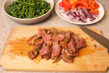 Marinated meat pieces arranged on a wooden cutting board with bowls of frozen green beans, sliced red pepper, and red onion in the background, ready for hearty homemade stew or skillet dinner recipes