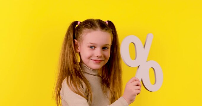 4K footage of a Caucasian girl holding her hands to form a percentage symbol against a yellow background, symbolizing math, discount, finance, or calculation concepts.