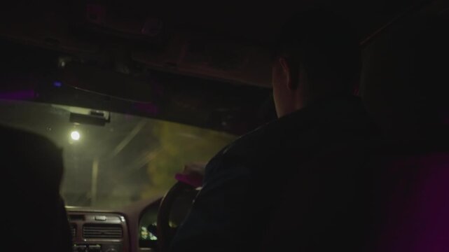 night city road white driver seen from rear, silhouette at wheel under stoplight glow. frames capture passing headlights, blurred signs, passenger shadow in backseat, cautious turns at intersection.