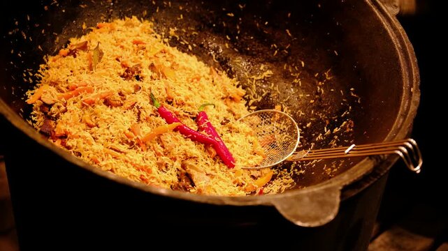 Traditional cooked rice dish with meat, carrots, and chili peppers in a large metal pot for serving