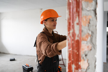 Construction worker woman in hardhat measuring concrete wall during home renovation work