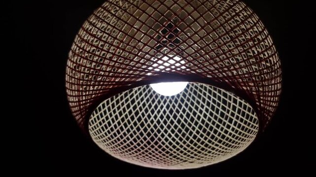 Woven pendant lamp with a two-tone lattice design glows against a black background. The intricate grid pattern creates a soft, diffused light, casting a warm ambiance.