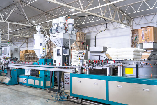 Plastic extrusion manufacturing machine in modern industrial factory, automated polymer processing line for plastic products production with raw material and control panels.