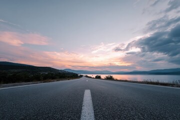 Fototapeta premium Serene sunset over empty road by lake with mountain horizon and pink sky