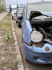 Old Neglected Vehicle Scene, Rusty Compact Vehicle With Broken Signals And Deflated Tire, Dilapidated Blue Hatchback Neglected Outside With Damaged Front And Worn Appearance