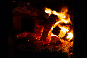 Bright flames flicker and crackle in a fireplace, casting a warm glow in the room while wood burns slowly on a chilly night
