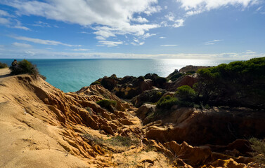 Golden rocks meet the tranquil blue sea under a partly cloudy sky, showcasing the beautiful coastline of malta