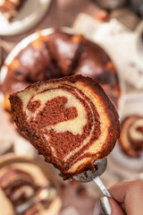 A piece of chocolate marble bundt cake or zebra cake with chocolate glaze on a spatula, brown table background, close up