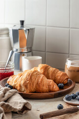 Delicious breakfast with croissants on wooden tray and coffee on white kitchen table background, text space