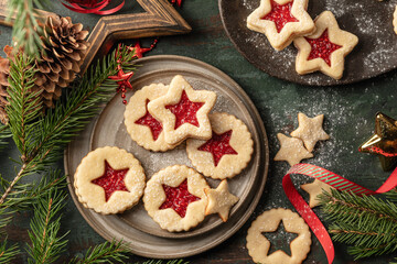 Homemade Linzer Christmas cookies filled with raspberry jam and dusted with sugar on ceramic plate with fir tree branches on wooden table top view