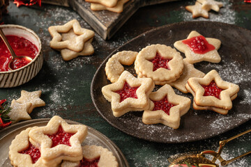 Homemade Linzer Christmas cookies filled with raspberry jam and dusted with sugar on ceramic plate with fir tree branches on wooden table
