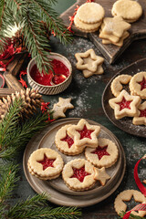 Homemade Linzer Christmas cookies filled with raspberry jam and dusted with sugar on ceramic plate with fir tree branches and festive decorations