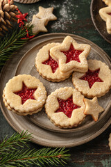 Homemade Linzer Christmas cookies filled with raspberry jam and dusted with sugar on ceramic plate close up with fir tree branches